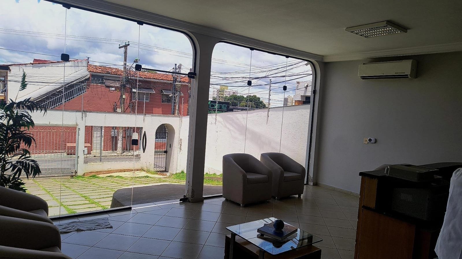 Sala de espera do escritório, com poltronas e ampla parede de vidro voltada para a rua